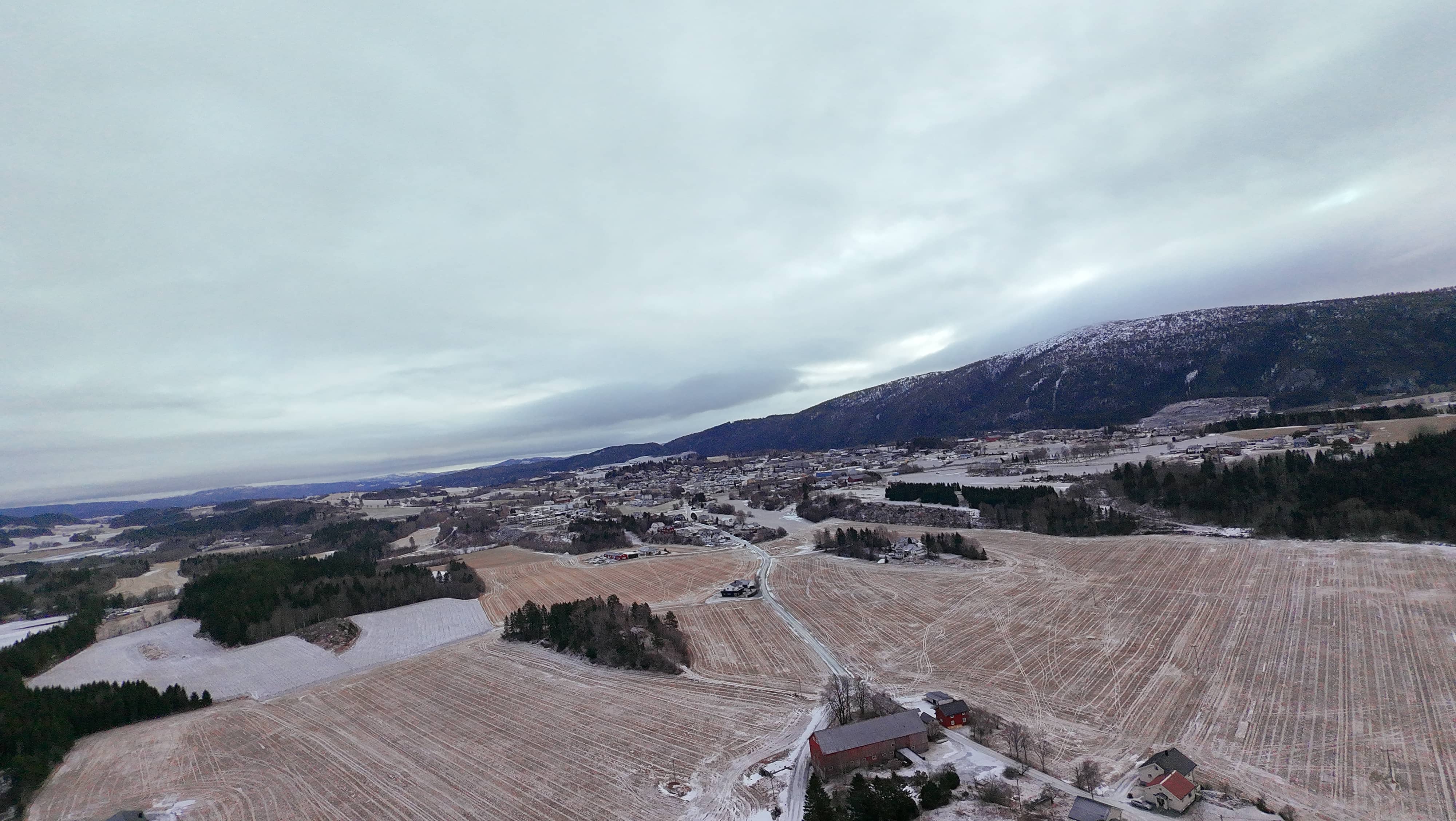 Panoramisk luftbilde av Åsen-regionen som viser typisk norsk landsbygd med jordbruksland, skoger og fjellbakgrunn